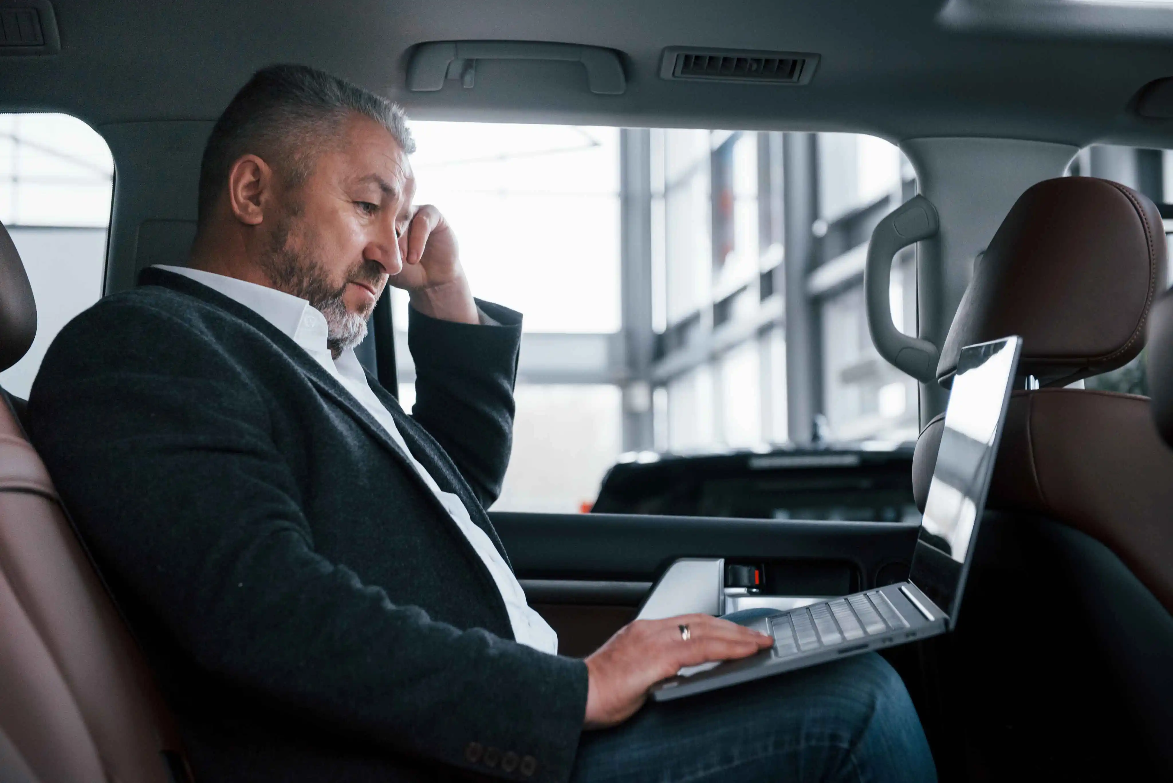 A business traveller taking a call with a laptop open in the back seat of a chauffeured car